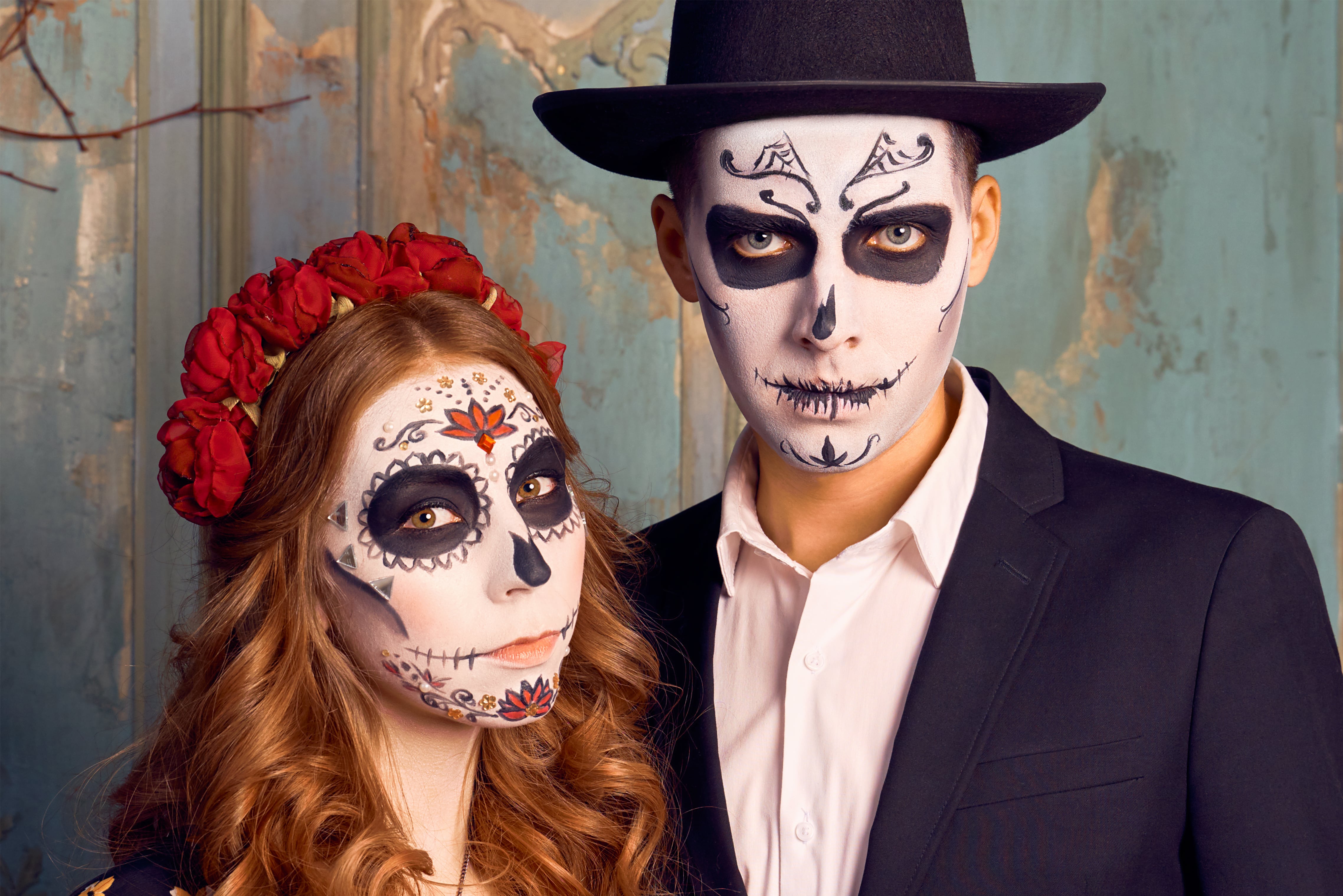 Indoor shot of serious romantic couple pose before Halloween event. People preparing for the popular carnival, dressed in costume, applied makeup in the shape of skull. Day of dead holiday in Mexico.