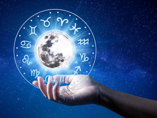 Una mano sostiene los 12 signos del zodiaco dentro de un horóscopo circular